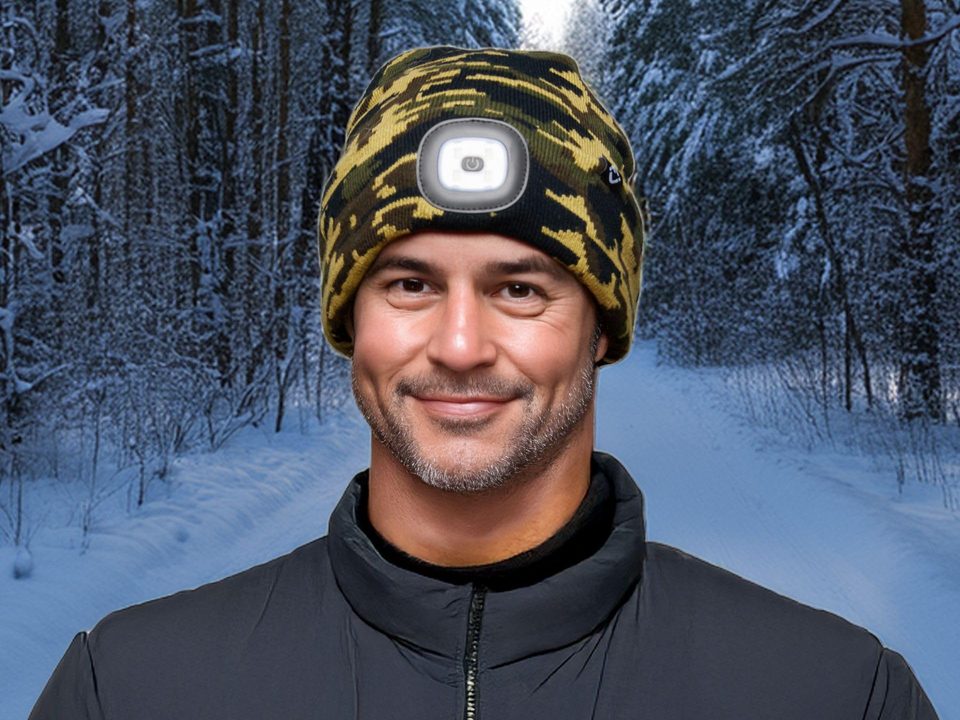 A smiling man on a snowy forest trail wearing the LED Light Rechargeable Headlamp Beanie in Camo