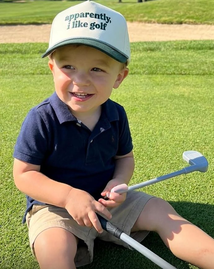 A toddler on a putting green wearing The Mini Caddie in Apparently, I Like Golf